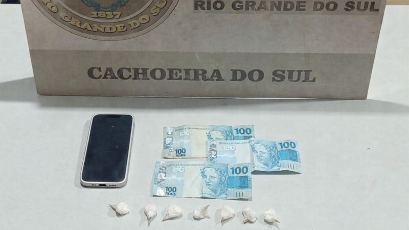 Sobre uma mesa est&aacute;o os materiais apreendidos: 07 por&ccedil;&otilde;es de coca&iacute;na (11,2 gramas);
01 celular iPhone;
01 motocicleta Honda/Titan;
R$ 305,00 em dinheiro.