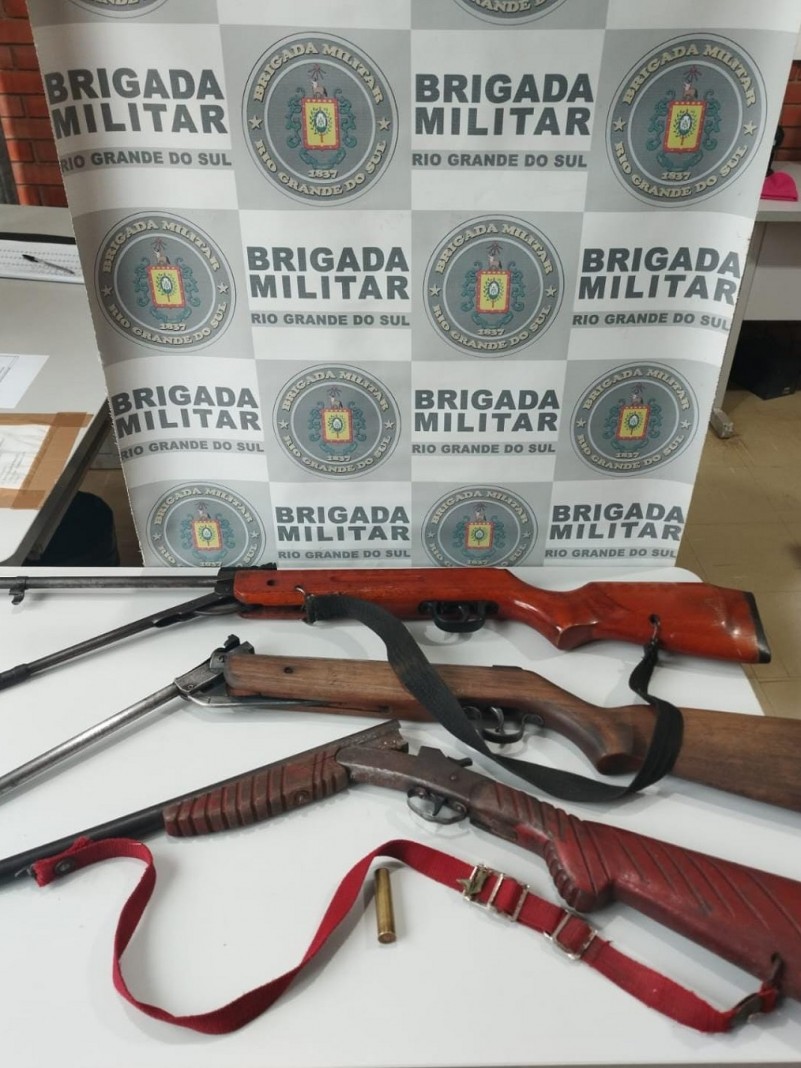 Sobre uma mesa est&atilde;o uma carabina de press&atilde;o sem marca e sem numera&ccedil;&atilde;o aparente, adaptada para calibre .22; uma carabina de press&atilde;o calibre 4.5, marca Rossi; uma espingarda calibre 32 sem numera&ccedil;&atilde;o cadastrada; al&eacute;m de uma muni&ccedil;&atilde;o calibre 32 n&atilde;o deflagrada