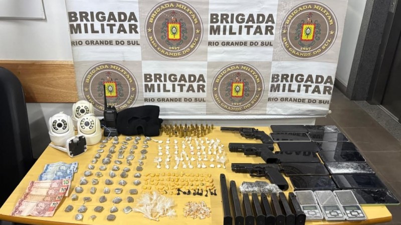 Materiais apreendidos durante a opera&ccedil;&atilde;o: armas, celulares, por&ccedil;&otilde;es diversas de drogas, todos dispostos em mesa.