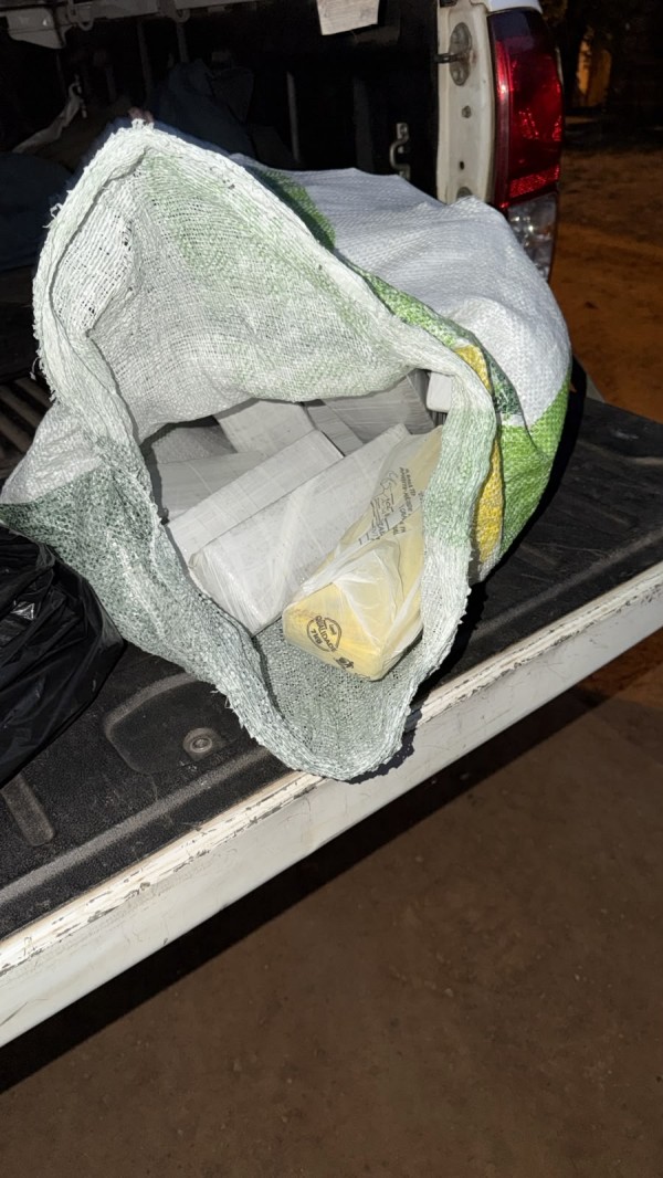 Tabletes de maconha e de cocaína dentro de plásticos em um saco de estopa aberto sobre um veículo. 