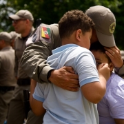 Policial Militar recebe o cumprimento de duas crian&ccedil;as com um abra&ccedil;o emocionado. 